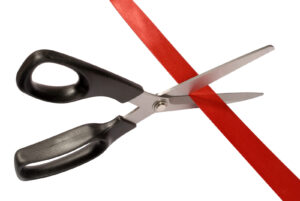Close-up of scissors cutting red ribbon or tape against a white background